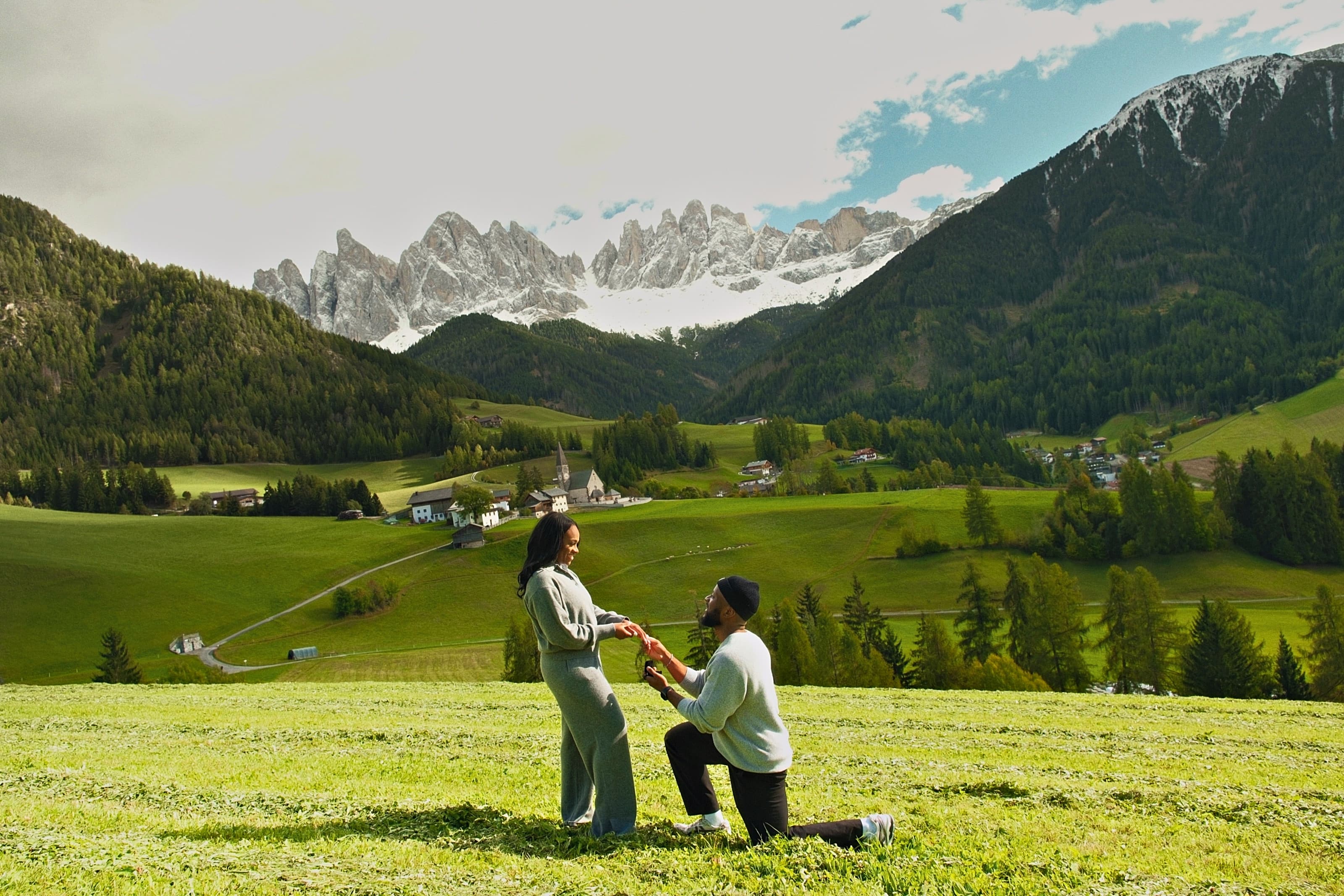 Donnel on one knee, proposing to Princess in a meadow below the Dolomites